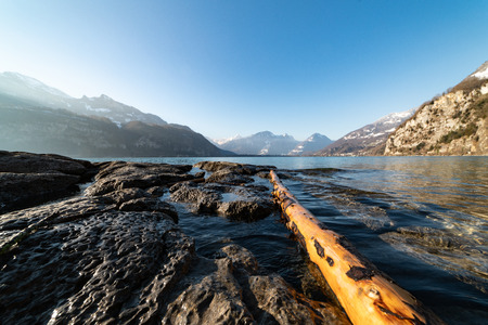 A washed up, debarked tree trunk swims between rocks in a mountain lake.の写真素材