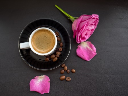 coffee with pink rose on dark leather surface with coffee beans