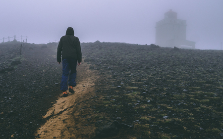 guy walking up a hill in iceland with a lot of fog lighthouseの写真素材