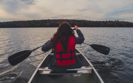 two girls canoeing with silver canoe on lake in canada algonquin national park on a sunny cloudy day during fallの写真素材