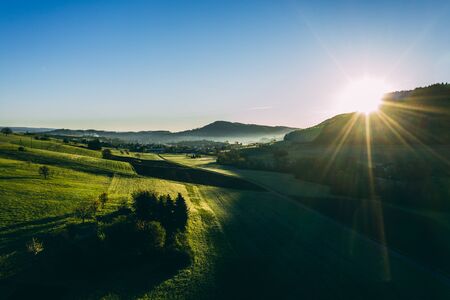 relaxing aerial shot of countryside village in switzerland during morning sun, beautiful sunny day with very green agricultural fieldsの写真素材