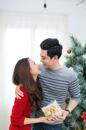Christmas Asian Couple. A handsome man giving her girlfriend/wife a gift at home celebrating New Year Peopleの写真素材