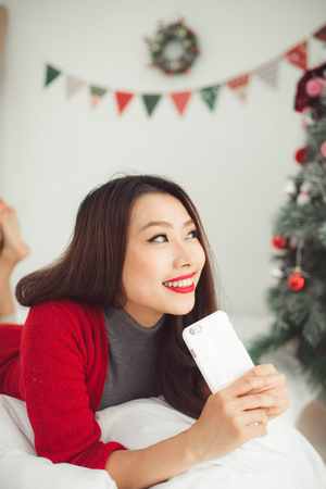 Happy young asian woman  holding a gift near christmas tree celebrating New Yearの写真素材