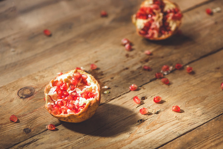 Falling down ripe pomegranate with cracks and splashes of juice and seeds wooden vintage background.の写真素材