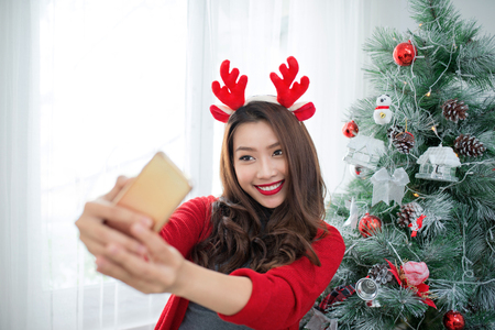 Happy young asian woman  taking a selfie photo near christmas tree at home celebrating New Yearの写真素材