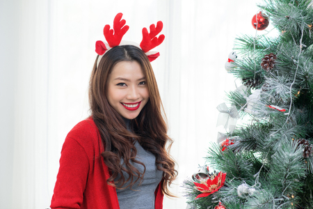Happy young asian woman  standing near christmas tree at home celebrating New Yearの写真素材