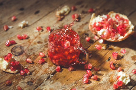 Ripe pomegranate with cracks and splashes of juice and seeds wooden vintage background.の写真素材