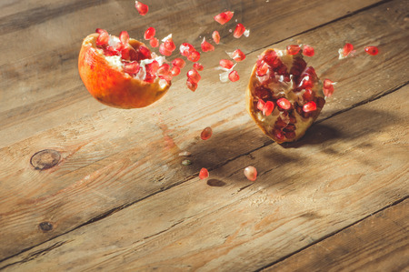 Falling down ripe pomegranate with cracks and splashes of juice and seeds wooden vintage background.の写真素材