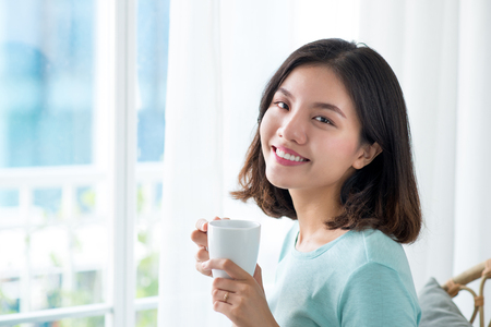 Young pretty woman sitting at opened window drinking coffee and looking outside enjoys of restの写真素材