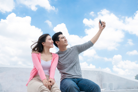 Young beautiful woman and asian man laugh against the dark blue sky with cloudsの写真素材