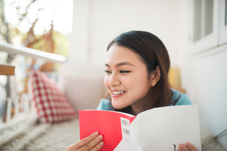 Portrait of young asian woman reading book at homeの写真素材