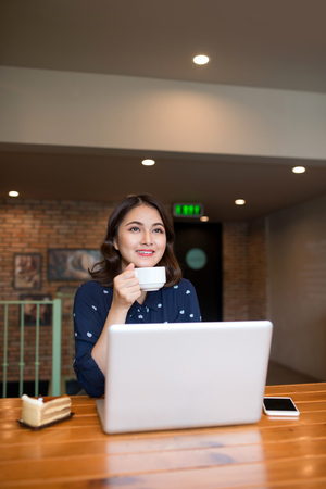Beautiful cute asian young businesswoman in the cafe, using laptop and drinking coffee smilingの写真素材