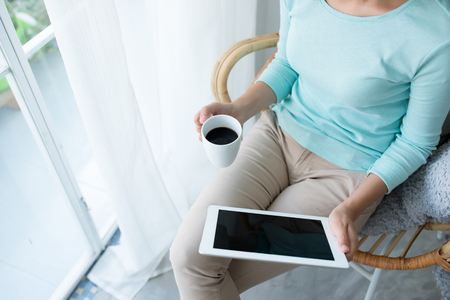 Beautiful asian young woman relaxing and using digital tablet at homeの写真素材