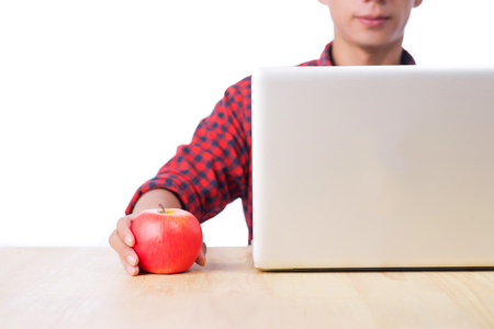 Cropped image of male studio using laptop with red apple at desk.の写真素材