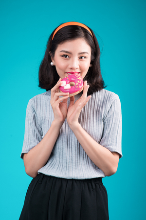 Asian beauty girl holding pink donut. Retro joyful woman with sweets, dessert standing over blue background.の写真素材
