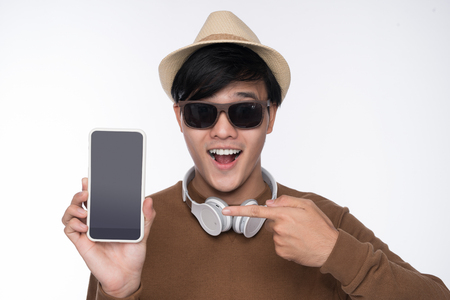 Smart casual asian man seated on chair, showing smartphone screen in studio backgroundの写真素材