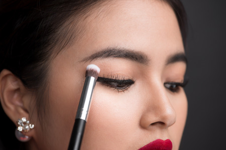 Close up of hand of asian woman applying eyeshadow on female eyelid.の写真素材