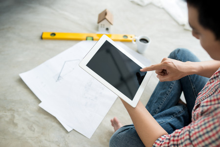 Young handsome male asian architect working at home using tablet on the floor.の写真素材