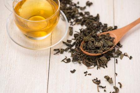 Black tea in a glass cup and tea leaves in wooden spoon on black stone background.の写真素材