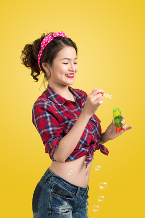 Pinup model blowing soap bubbles over yellow background.の写真素材