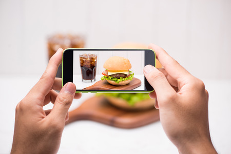 Hands hold smartphone taking photo of homemade BBQ burgerの写真素材