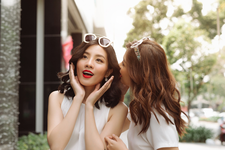 Woman whispering in her friends ears. Two excited friends shopping.