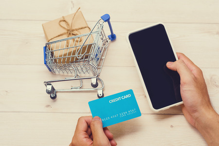 Shopping online concept. Small blue trolley and gadgets on the wooden table.の写真素材