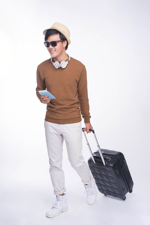 Full length of young asian man holding passport with suitcase over grey backgroundの写真素材
