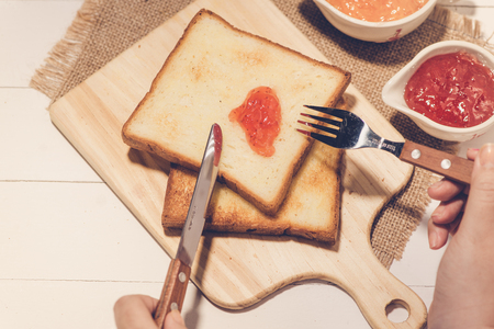Asian woman eating bread with strawberry jam for breakfast. Focus on hands.の写真素材