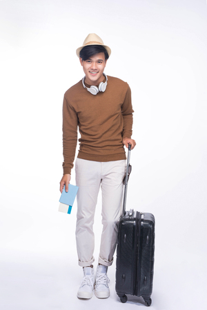 Full length of young asian man holding passport with suitcase over grey backgroundの写真素材