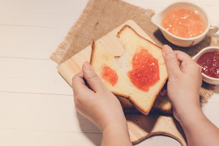 Asian woman eating bread with strawberry jam for breakfast. Focus on hands.の写真素材
