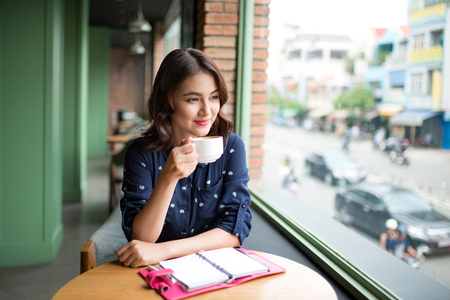 Portrait of happy young business woman with mug in hands drinking coffee in the morning at restaurantの写真素材