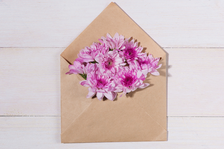 Blank white paper tag with brown envelope and pink flowers on wooden table.の写真素材