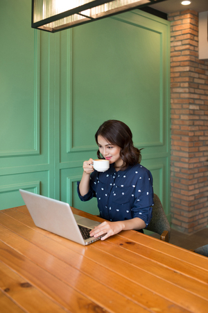Beautiful cute asian young businesswoman in the cafe, using laptop and drinking coffee smilingの写真素材