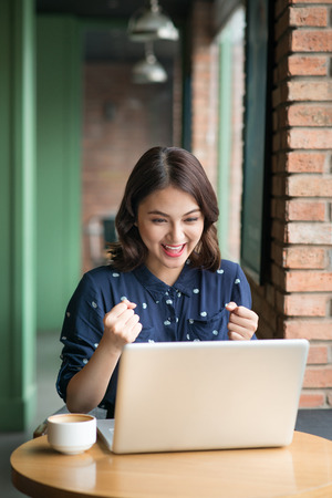 Beautiful cute asian young businesswoman in the cafe, using laptop and drinking coffee smilingの写真素材
