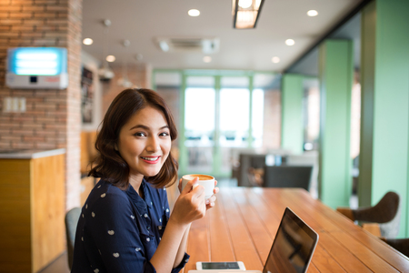 Portrait of happy young business woman with mug in hands drinking coffee in the morning at restaurantの写真素材