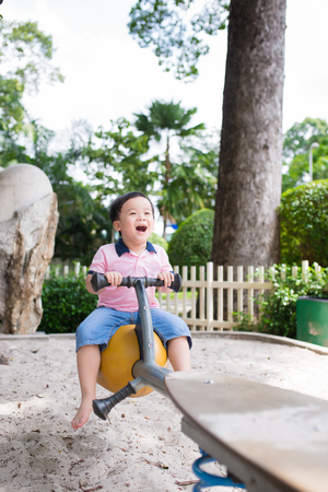 Happy asian boy playing seesaw at the playground in the parkの写真素材