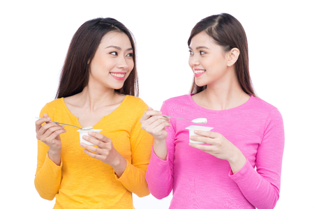 Two young beautiful woman eating yogurt as breakfast or snack. Isolated on whiteの写真素材