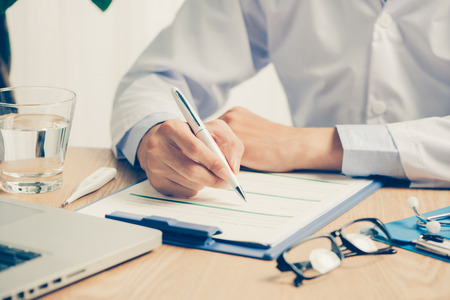 Male doctor working at wooden desk in clinicの写真素材