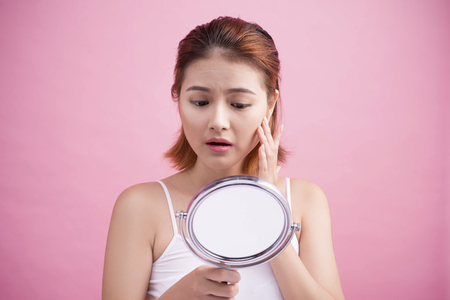 Pretty young asian woman holding a mirror, touch and worrying about her faceの写真素材