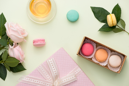 French macaroons. Many variegated sweet macarons in box with bouquet of pink roses on the tableの写真素材