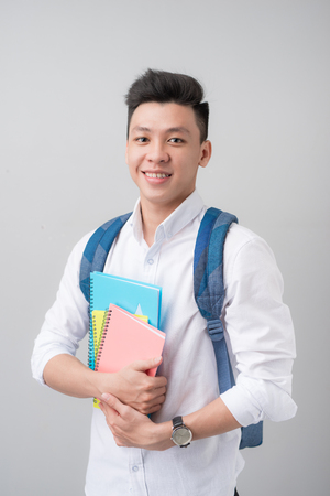 Happy casual asian male student holding books isolated on a gray backgroundの写真素材