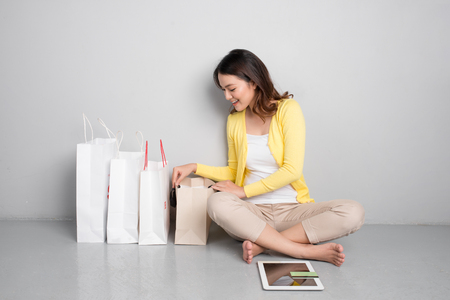 Young asian woman shopping online at home sitting besides row of shopping bagsの写真素材