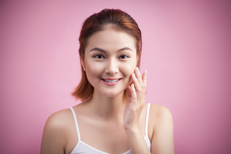 Portrait of a beautiful smiling young woman with natural make-up. Skincare, healthcare. Healthy teeth. Studio shot. Isolated on Pink Background.の写真素材