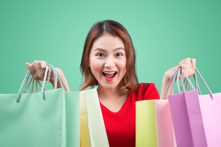 Beautiful young asian woman with colored shopping bags over blue backgroundの写真素材