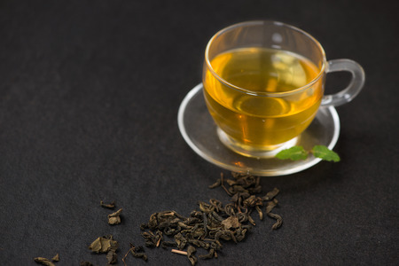 Black tea in a glass cup and tea leaves on black stone background.の写真素材