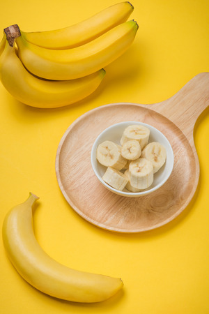 A banch of bananas and a sliced banana in a dish over yellow backgroundの写真素材