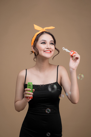 Playful pinup woman blowing party bubbles over yellow backgroundの写真素材