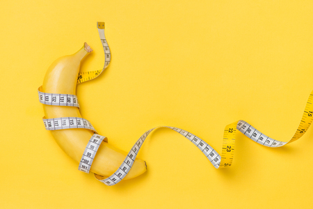 Diet, fitness and health concept presented by yellow banana wrapped in measure tape isolated on yellow paper backgroundの写真素材