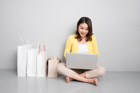 Young asian woman shopping online at home sitting besides row of shopping bagsの写真素材